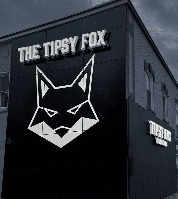 The Tipsy Fox black ACM-clad building corner with illuminated logo signage at dusk